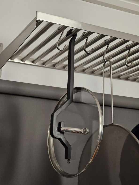 A pot lid suspended from a rack via a 3D-printed hook. The rack also holds other pots and pans.