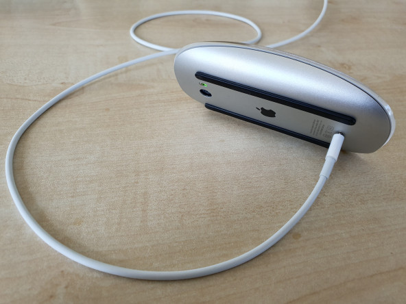 An Apple Magic Mouse tilted on its side, charging